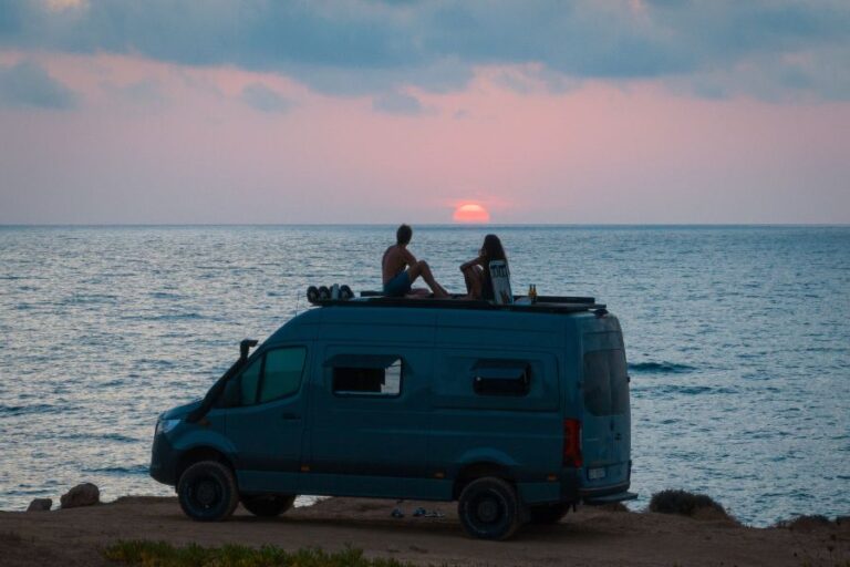 Furgone camperizzato al tramonto in riva al mare, coppia seduta sul tetto: lo stile di vita di chi fa smart working in camper