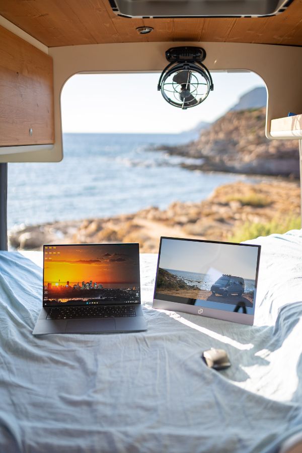 Postazione di lavoro con laptop e monitor secondario dentro un furgone camperizzato, vista sul mare, esempio di smart working in camper